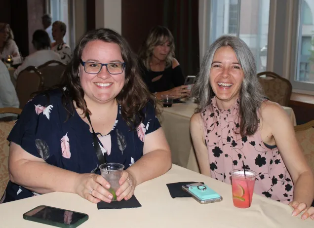 two women smiling and holding drinks at a table