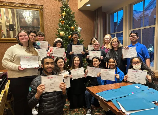 group of children holding up sheets of paper in front of a christmas tree